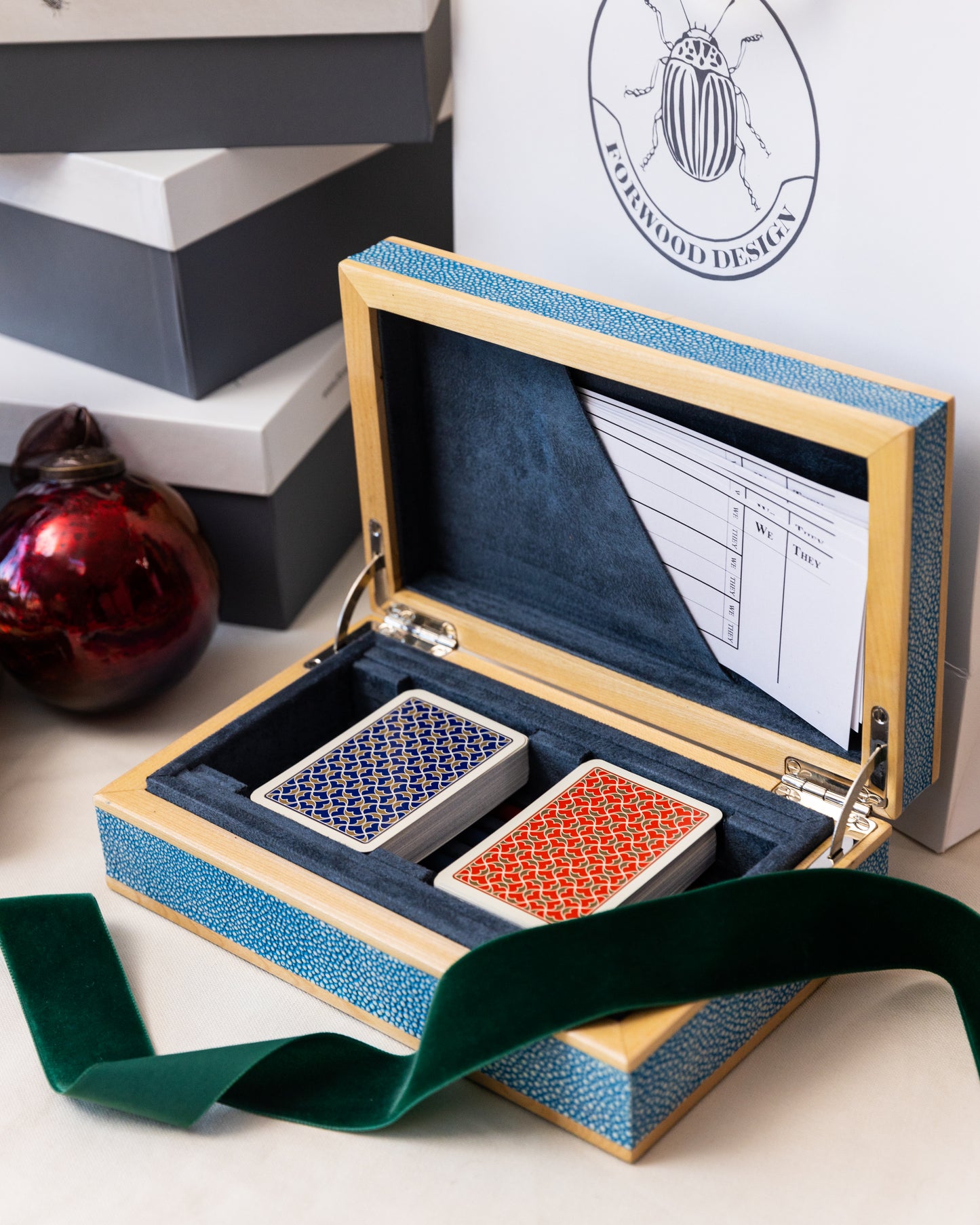 A luxury bridge set presented in a teal shagreen case with a sycamore wood trim, open to show playing cards, pencils, and score sheets inside.