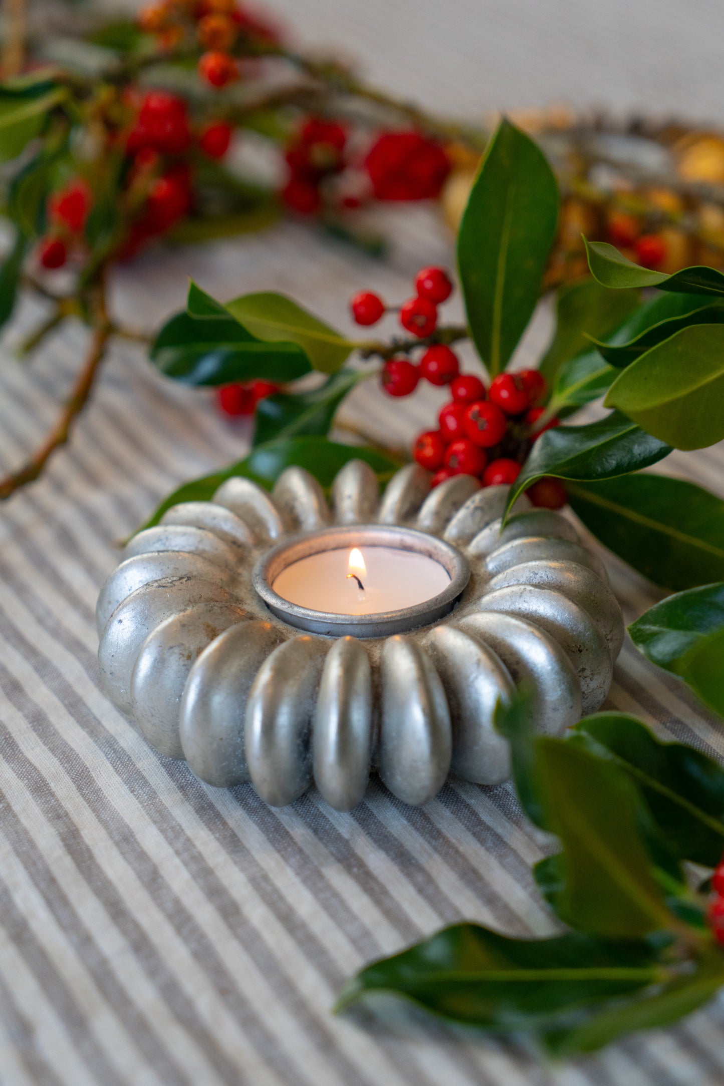 A silver tea light holder in the shape of a seed pod in a Christmas setting