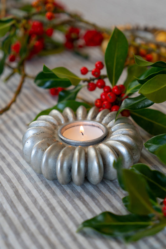 A silver tea light holder in the shape of a seed pod in a Christmas setting