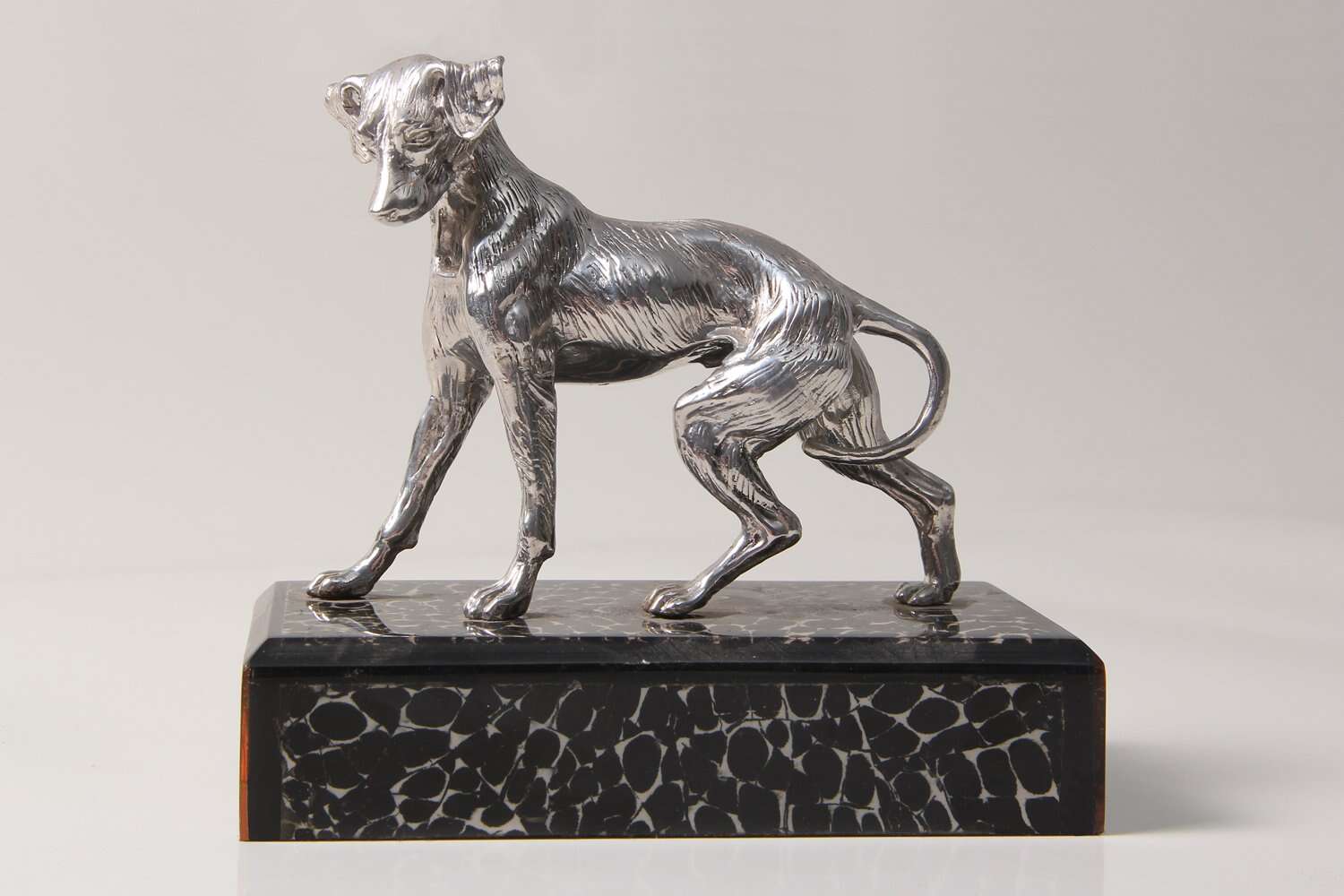 A stainless steel dog sculpture on a black-and-white eggshell plinth.